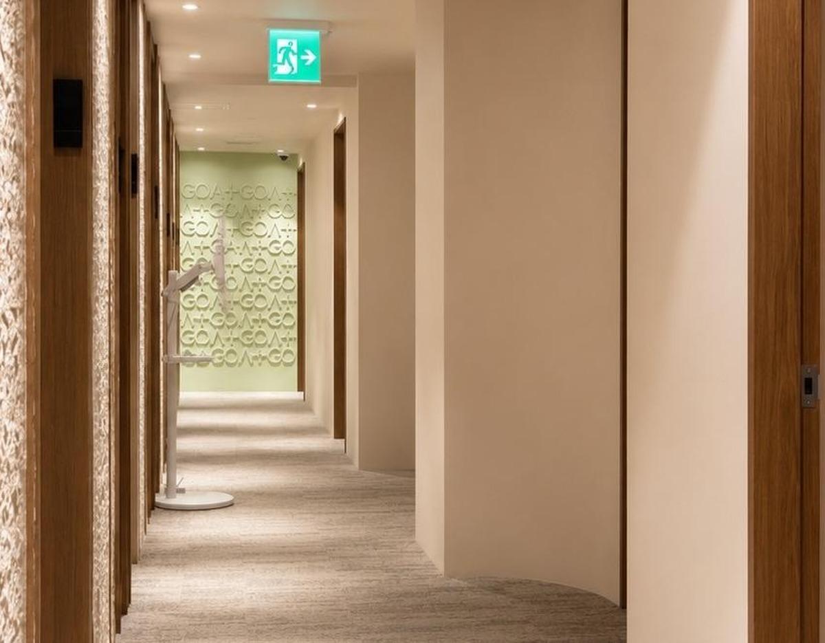GOAT clinic beige hallway with wooden door frames, textured wall panels and illuminated exit sign at far end