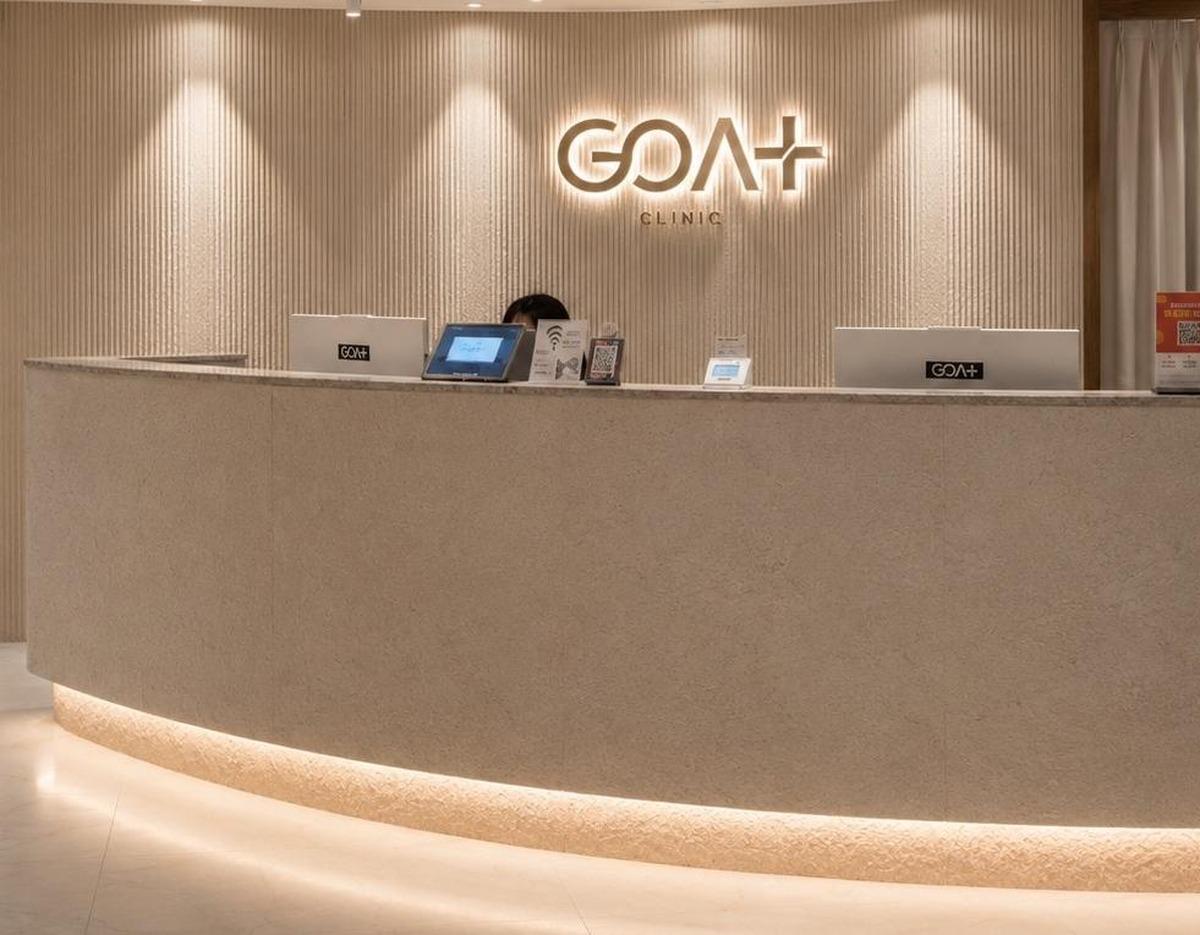Minimalist curved reception desk with illuminated GOAT Clinic logo on textured wall and tablet displays on counter