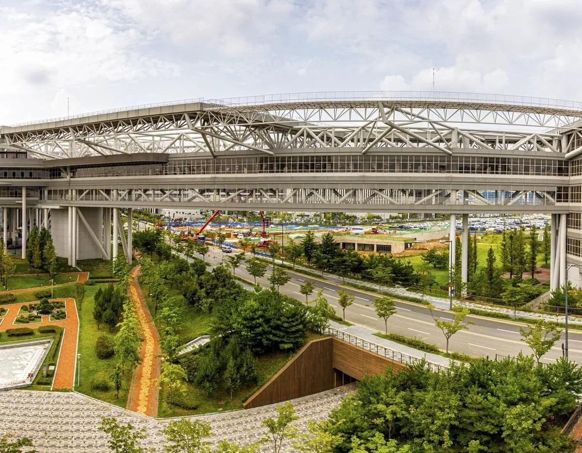 Government complex rooftop garden walkway with steel truss bridge above roads and landscaped green paths in Sejong.