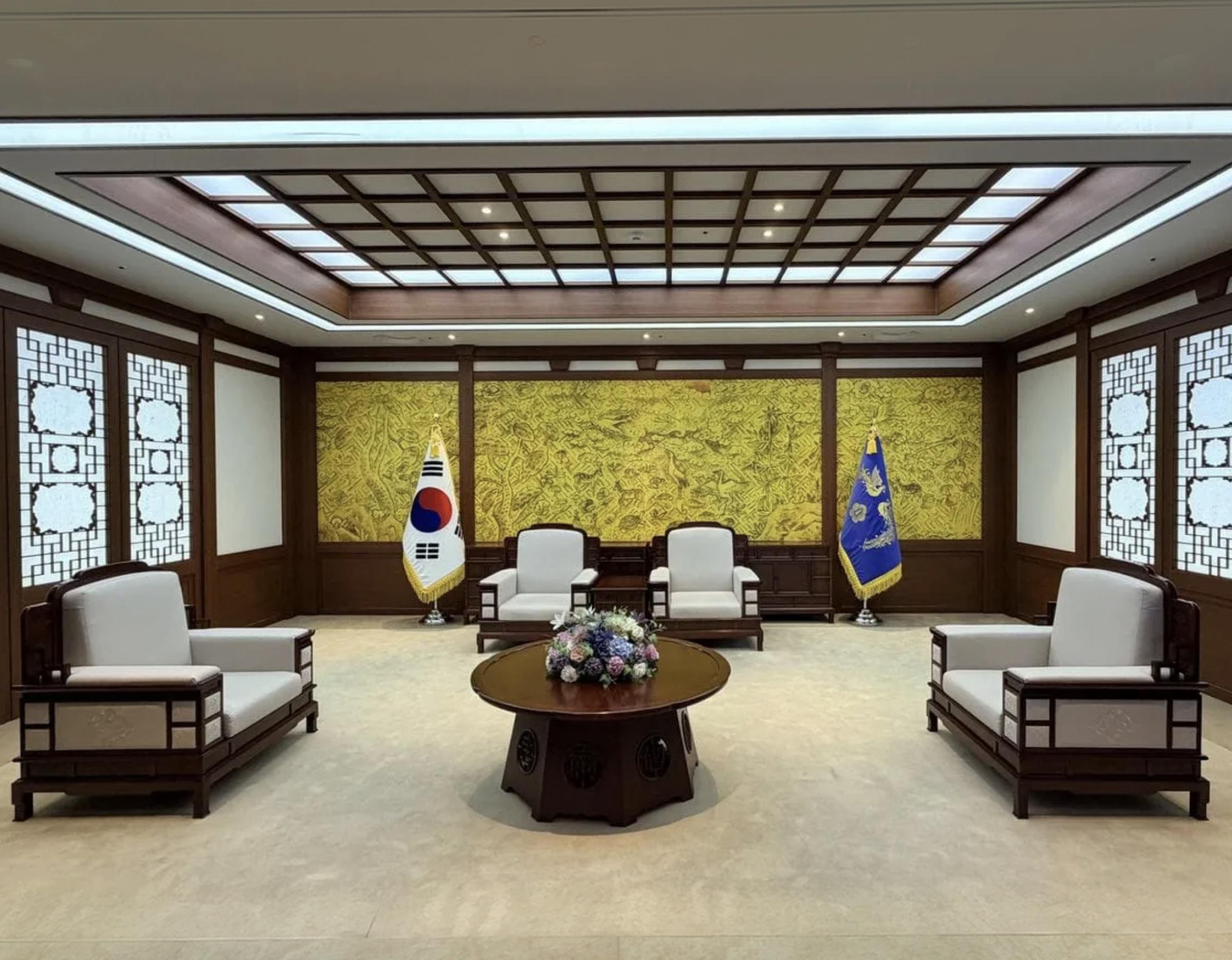 Sejong presidential reception room with low wooden table, four carved armchairs, Korean flag and blue presidential flag.