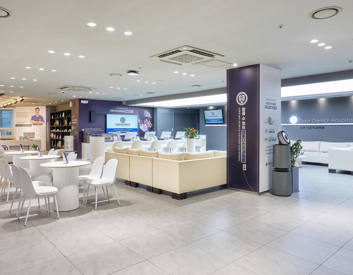 Bright modern dental clinic waiting area with white tables, chairs, cream sofas and reception desks at Sinchon Dain Dental Hospital.