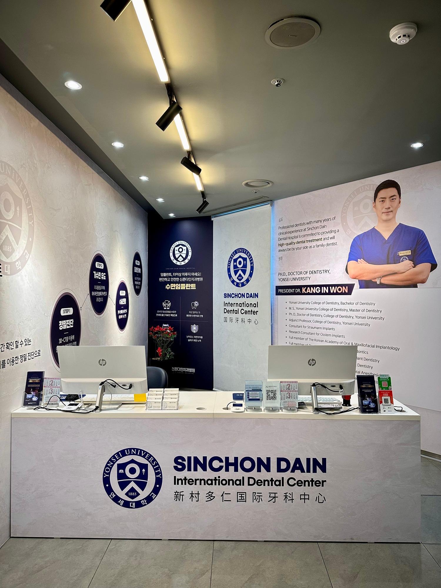 Reception desk of SINCHON DAIN International Dental Center with dual computer monitors, branded front desk and wall poster of dentist