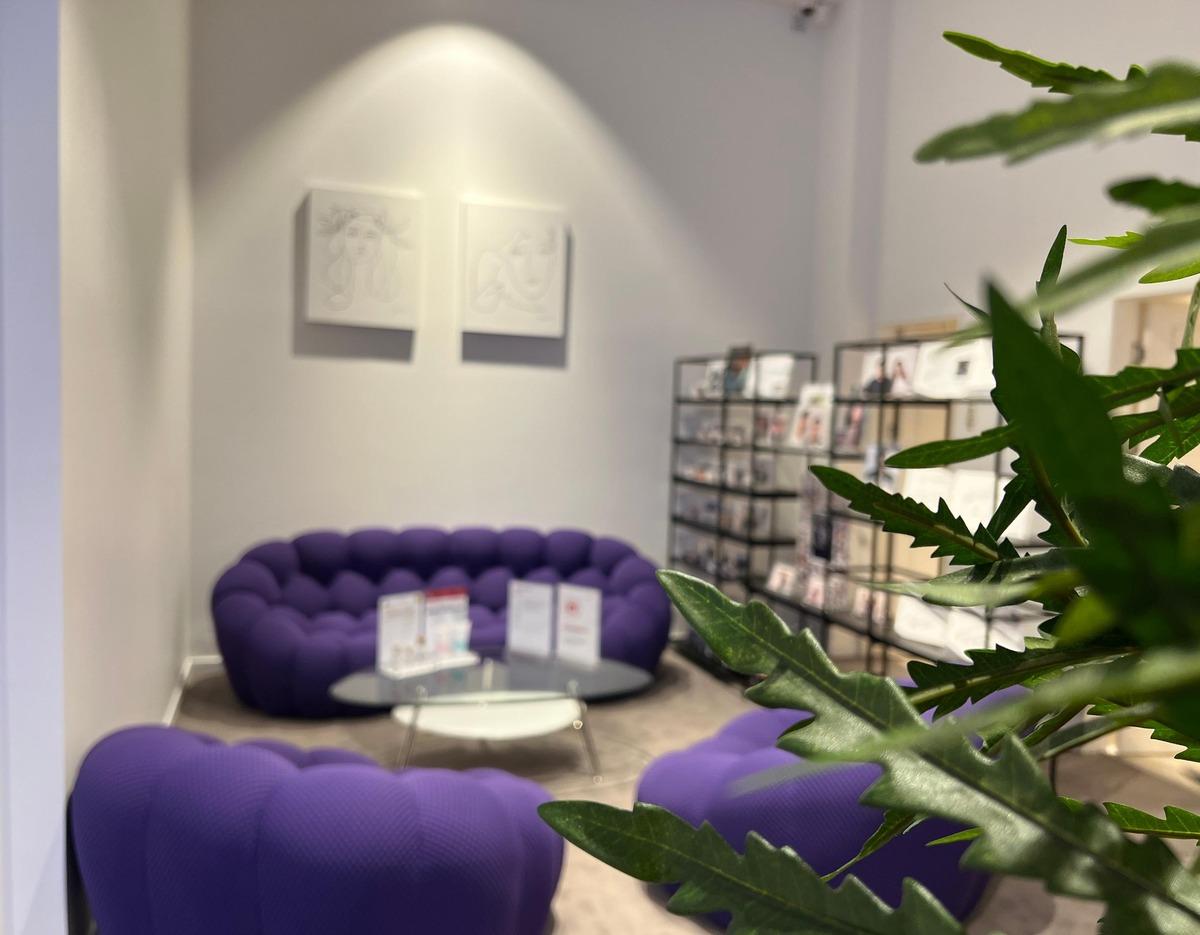 Waiting area with tufted purple sofas, glass coffee table with brochures and leafy plant in foreground.