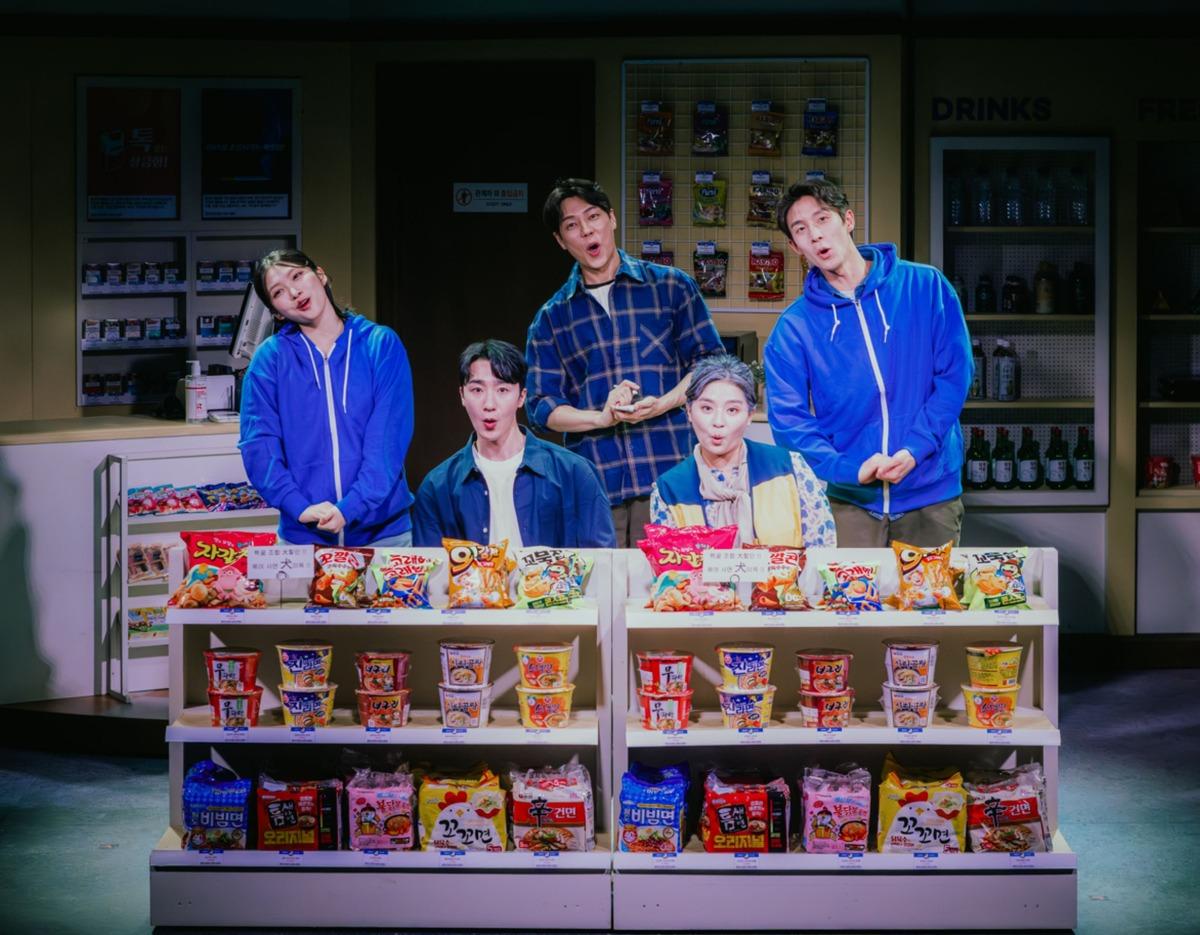 Busan Music Drama cast on convenience store set, five actors behind shelves of colorful snacks and instant noodles, mid-performance expressions
