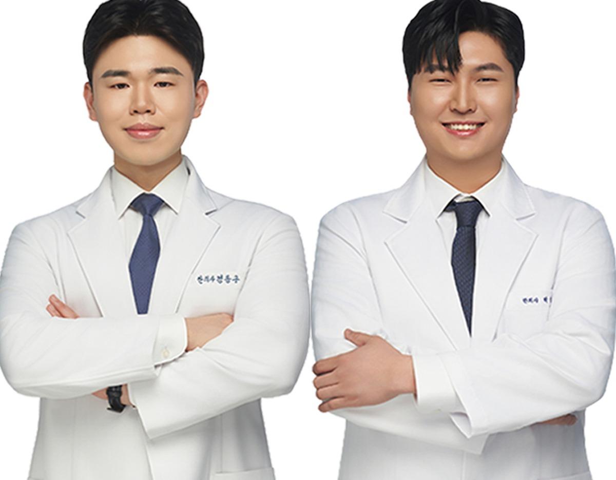 Two smiling men in white medical coats and dark ties standing side-by-side with arms crossed against a white background