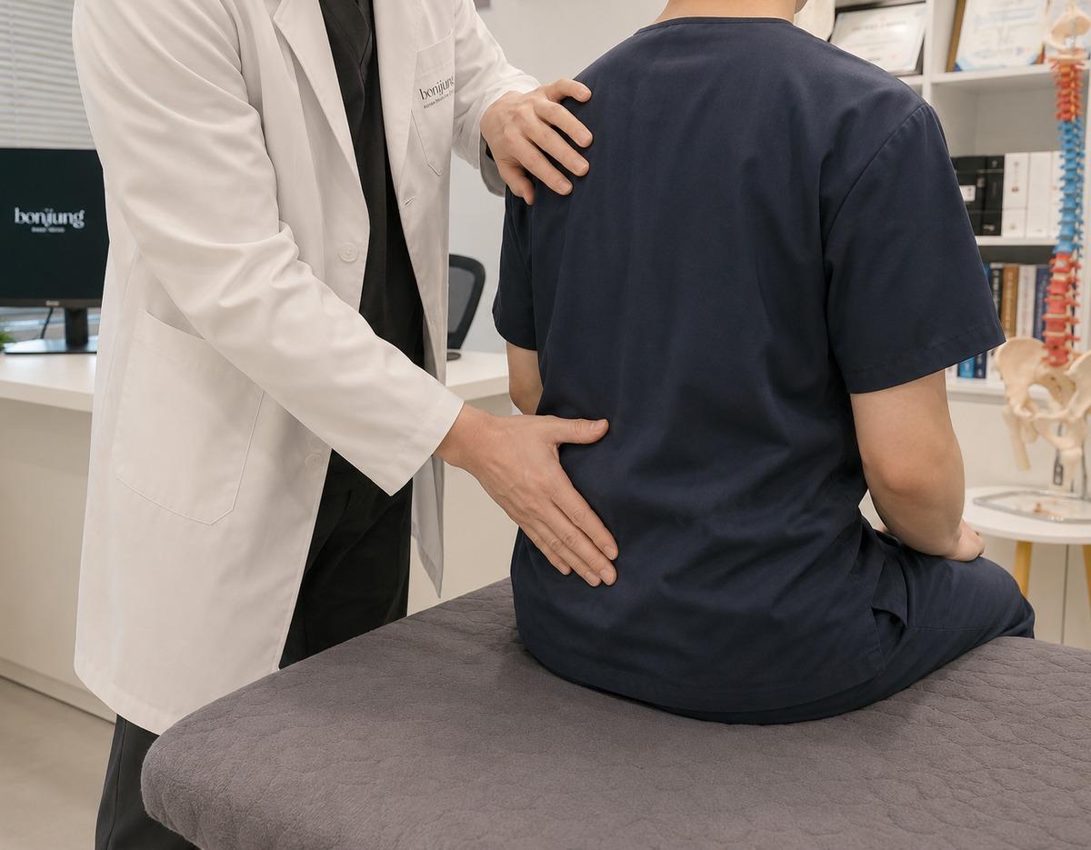 Doctor in white coat examining a patient's lower back while patient sits on an exam table at Bon Jung Korean Medicine Clinic