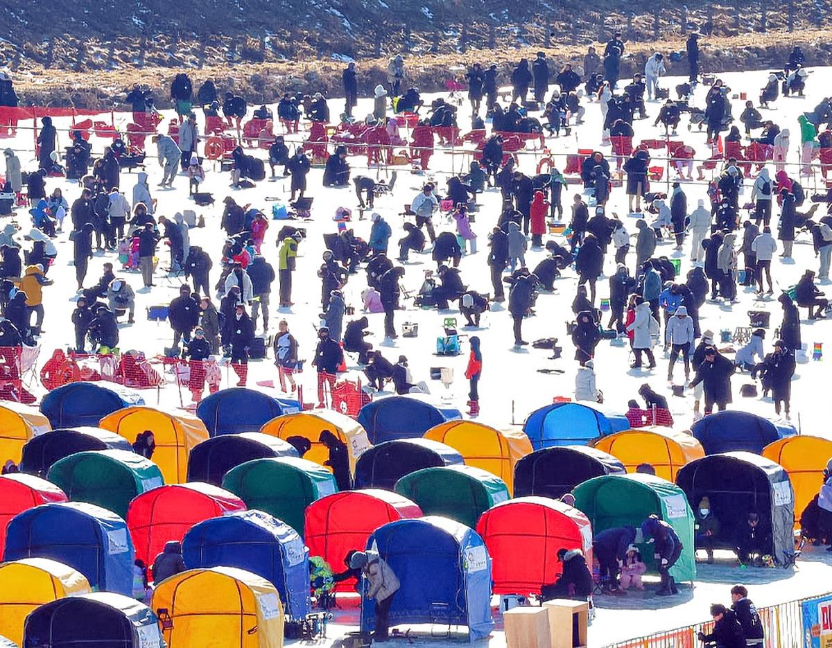 Crowded frozen lake at Pyeongchang Trout Festival with dozens of colorful fishing tents and people ice fishing and walking around