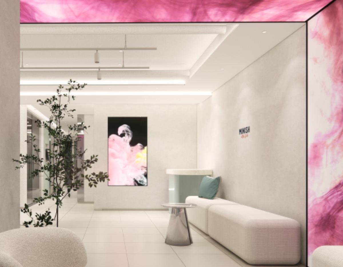 Minimalist dental clinic waiting area with long white sofa, small round table, green pillow and pink marble accent walls.