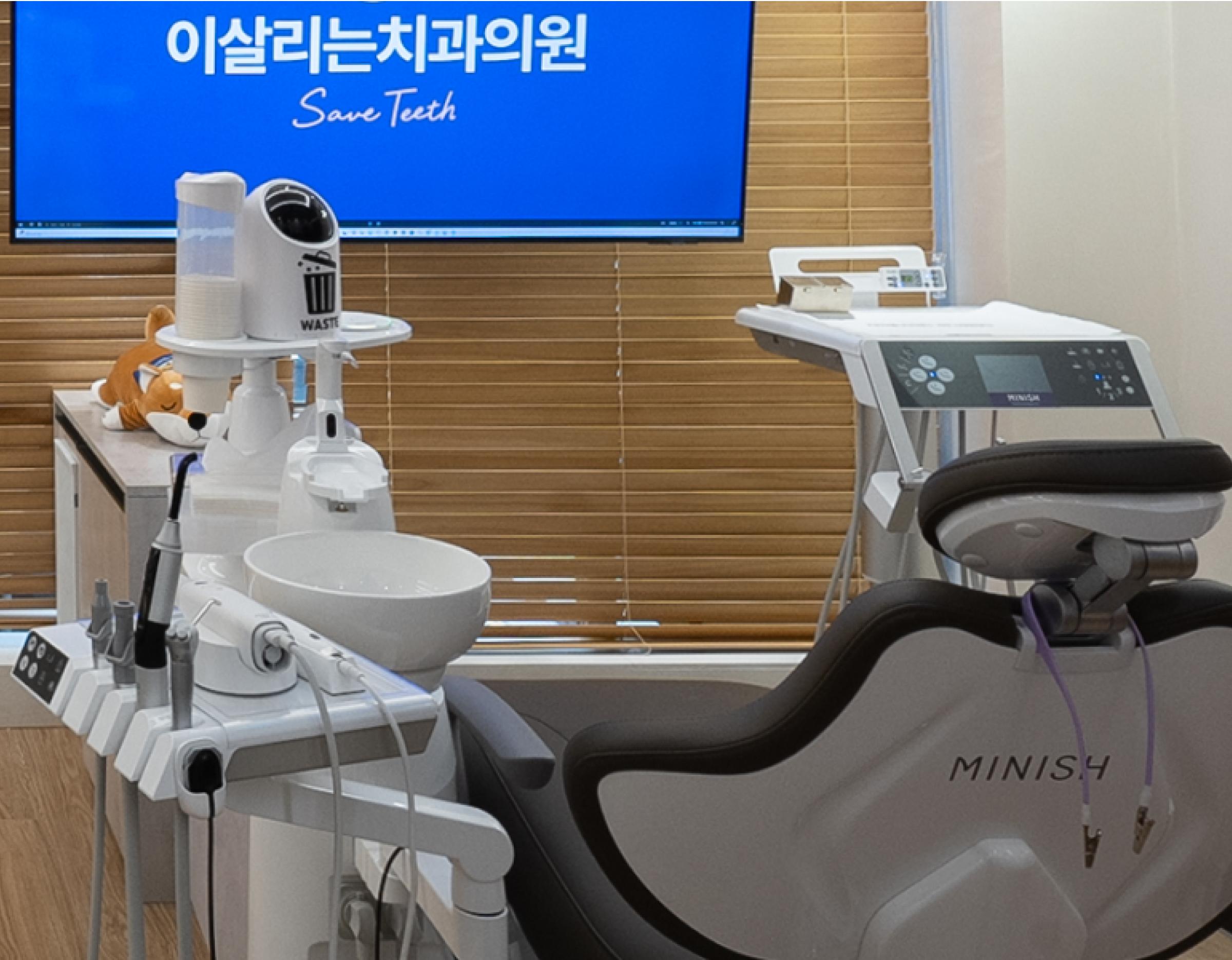 Dental treatment room with a Minish dental chair, instrument tray, sink, monitor showing "Save Teeth" in Korean and English