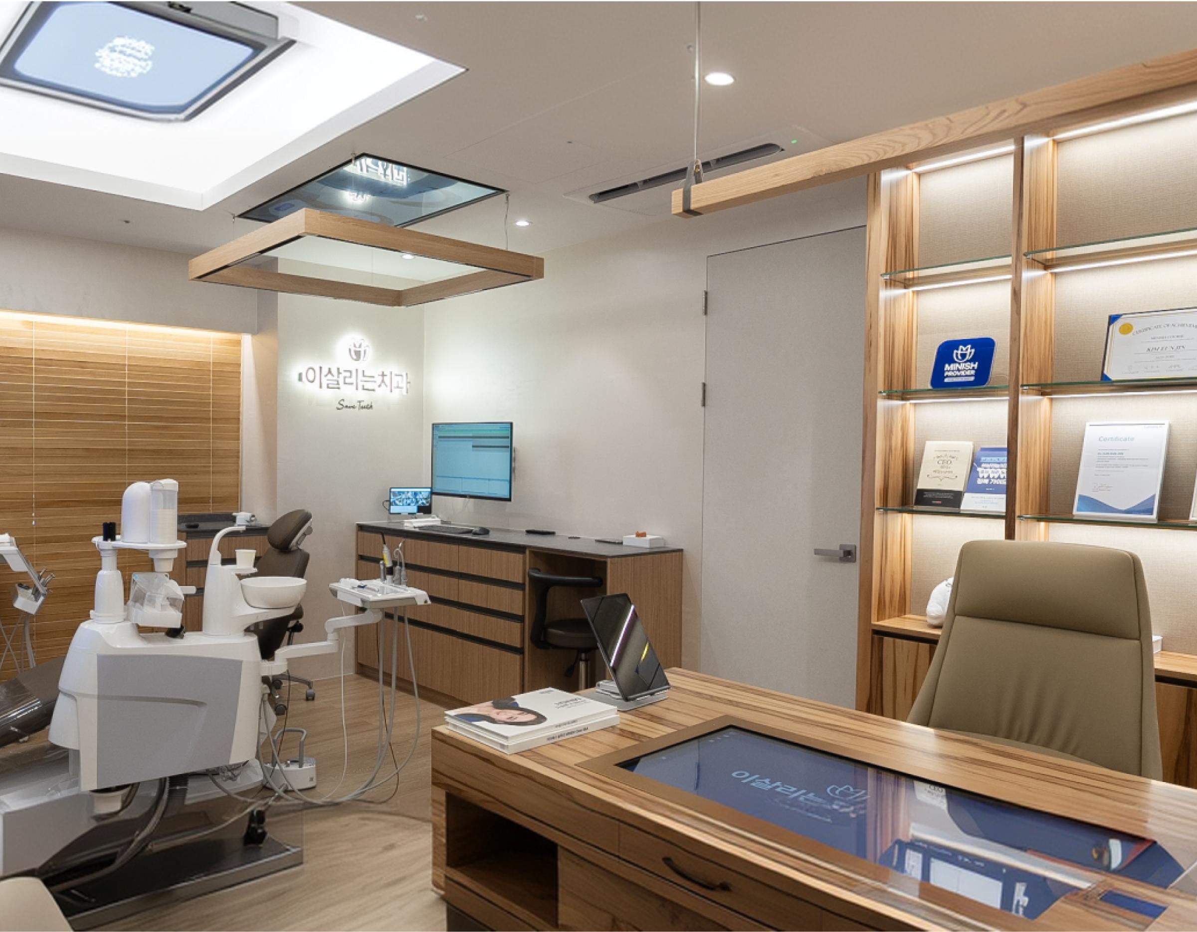 이살리는치과의원 신논현역 dental clinic private treatment room with modern dental chair, wooden desk and illuminated certificate shelves