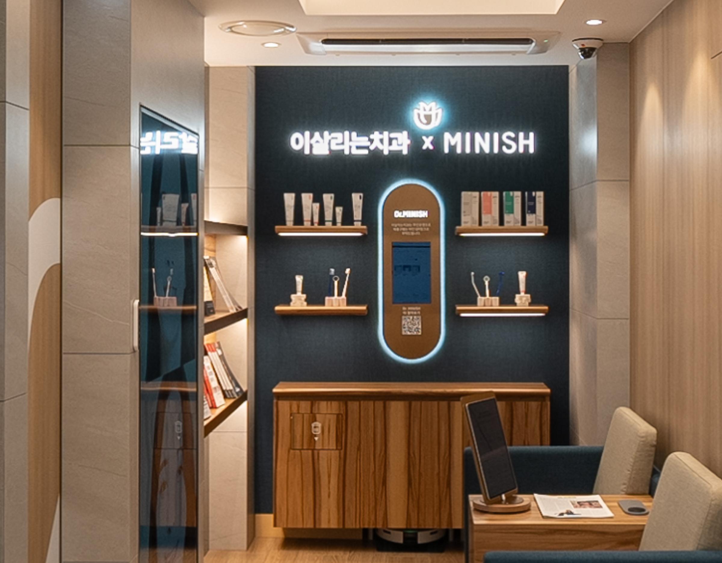 이살리는치과의원 신논현역 reception display wall with MINISH logo, wooden shelves holding dental products and seating area