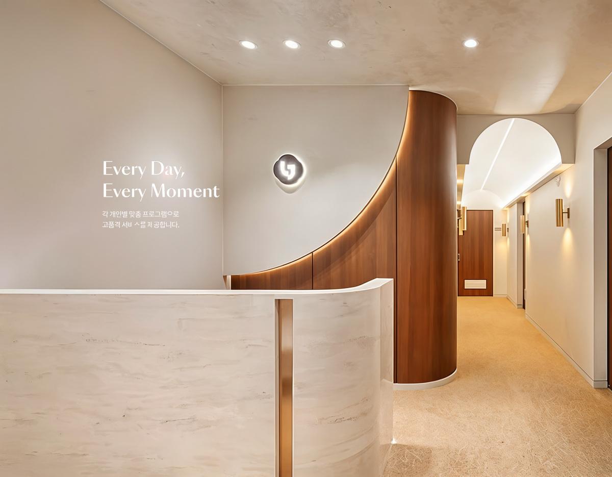 Minimalist clinic reception with curved white marble desk, warm wood paneling, soft lighting and hallway to treatment rooms.