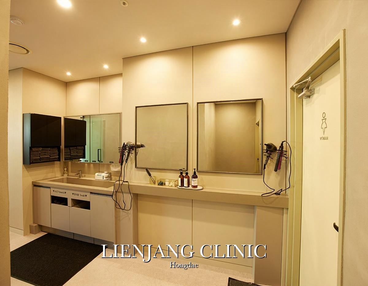 Minimalist beige clinic vanity with two mirrors, hairdryers, toiletries, towel cubbies and "LIENJANG CLINIC Hongdae" text.