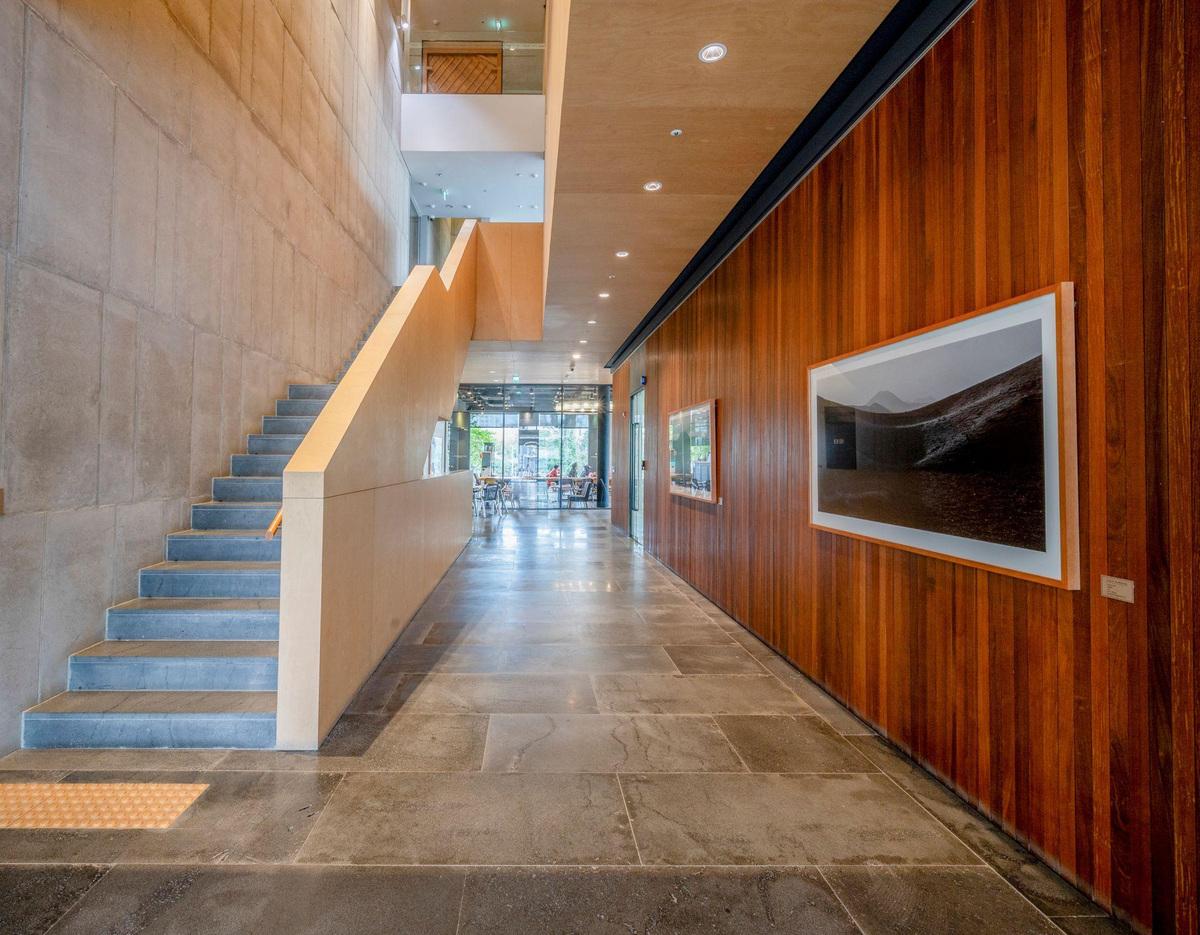 Clinic lobby with modern staircase on left, wood-paneled wall with framed artwork on right, polished stone floor.