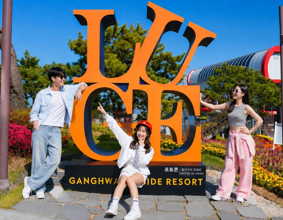 Three young people posing around large orange "LOVE" style sculpture at Ganghwa Seaside Resort entrance, woman wearing red helmet sitting center.