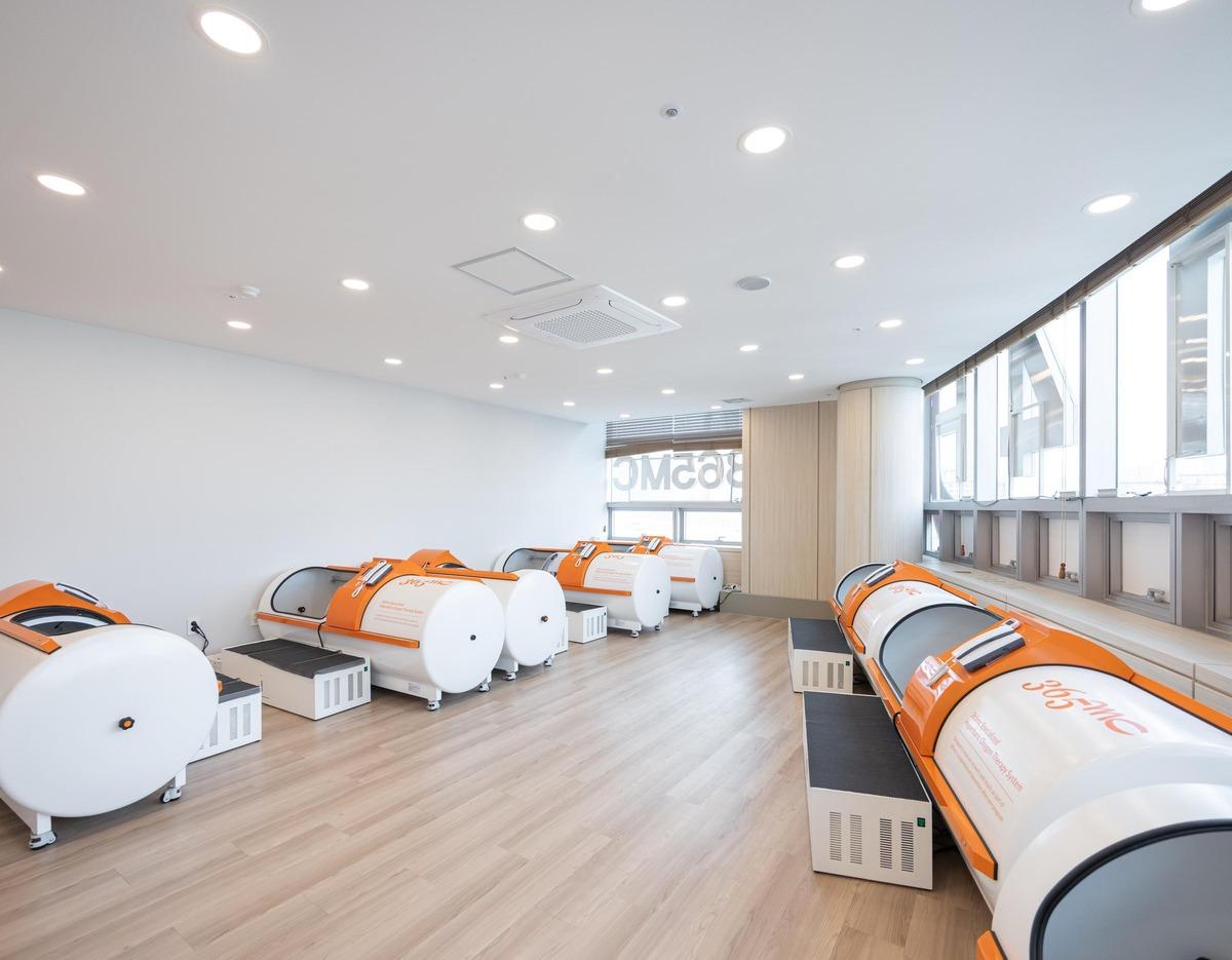 365mc병원 부산점 treatment room with row of white and orange hyperbaric-like body contouring pods along windows on wood floor