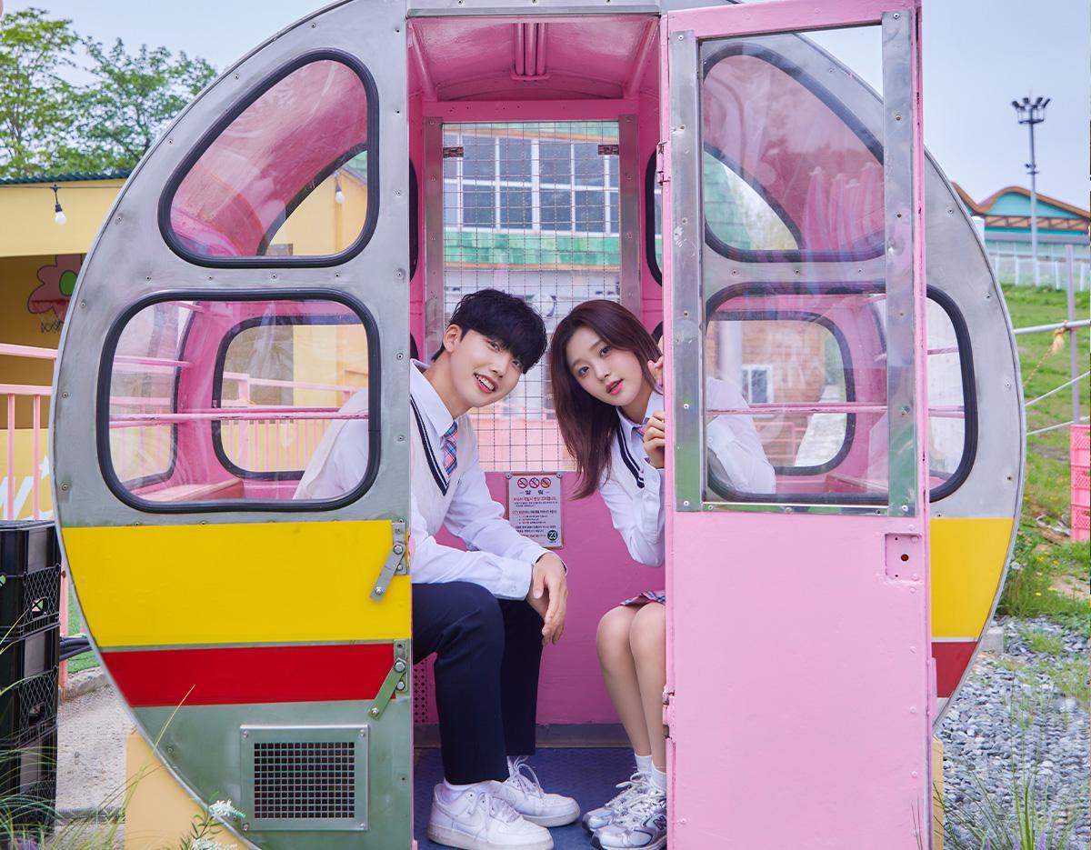 Two teenagers in matching school uniforms sitting inside a pink and yellow amusement park gondola at Gyeongju World.