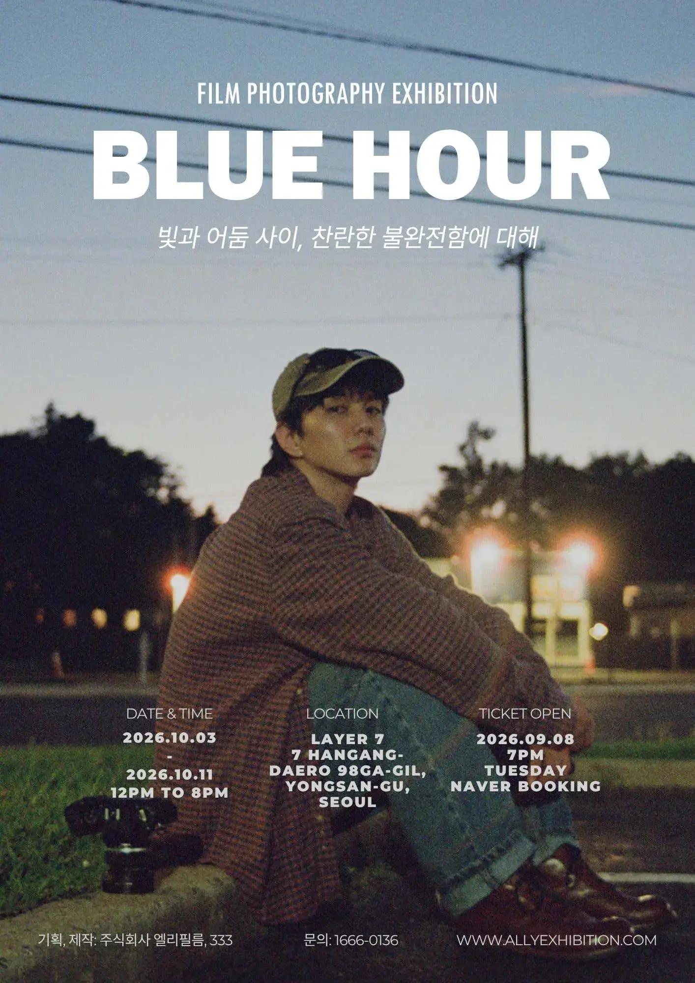 young person in a plaid coat and cap sitting on a curb at dusk with blurred streetlights and power lines behind, "BLUE HOUR" text above
