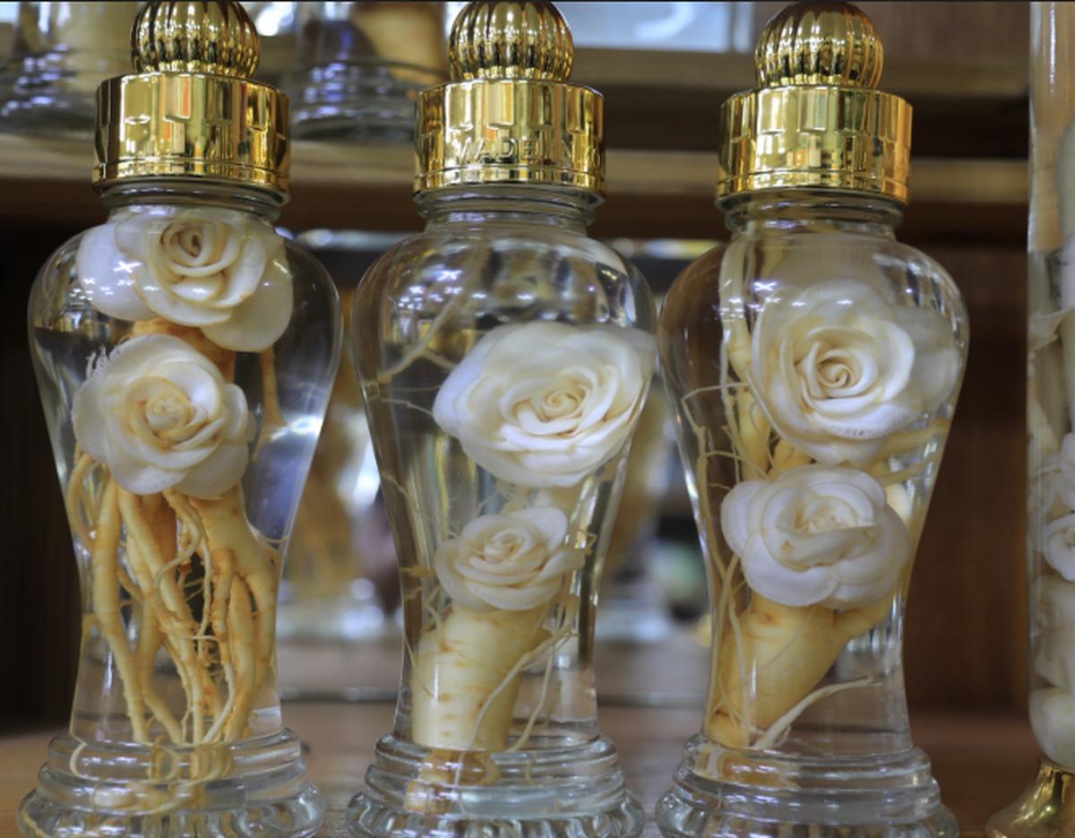 Three glass bottles of Geumsan ginseng liquor with sliced ginseng shaped like white roses and visible roots, gold caps.
