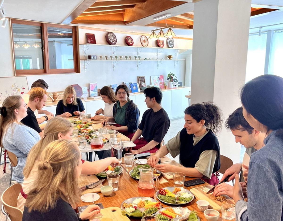 오미요리연구소 전통시장 투어 & 한식 쿠킹 클래스 participants seated around a wooden table sharing homemade Korean dishes and salads.
