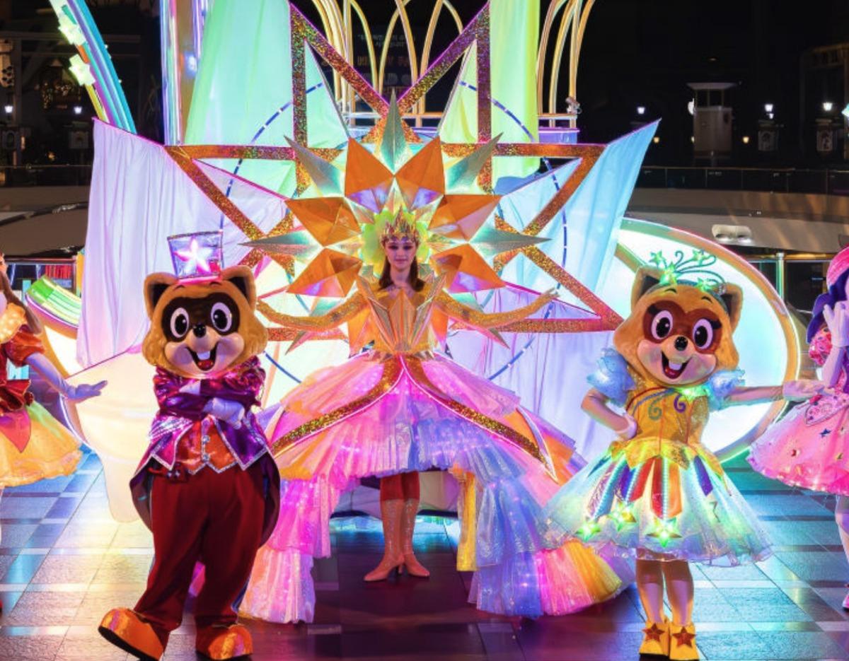 colorful nighttime parade scene with two raccoon mascots flanking a performer in a glowing starburst costume