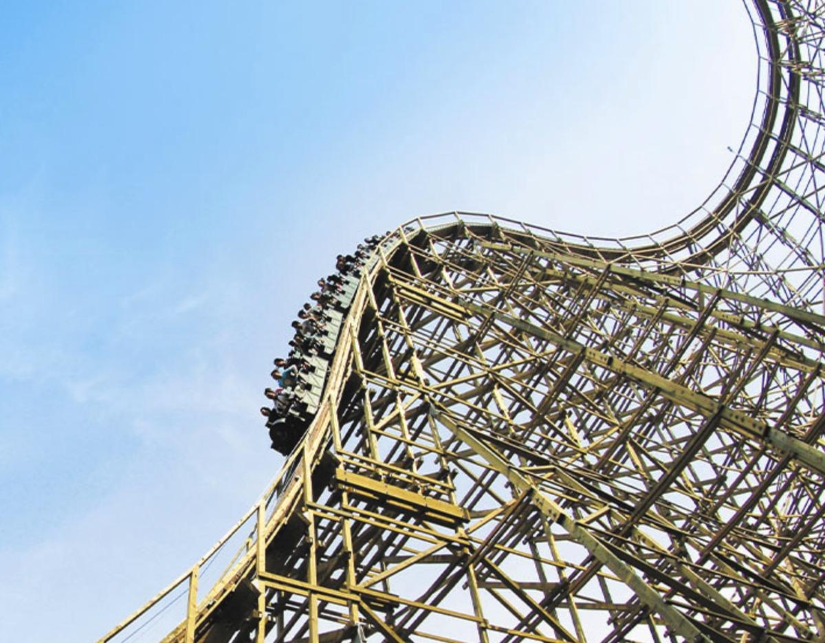 Wooden roller coaster structure with a train of riders cresting a steep drop against blue sky, Lotte World day 1.