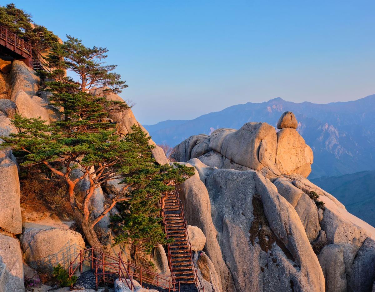 Ultrasanbawi granite summit and wooden stairway winding past pine trees on rugged Seoraksan ridgeline at sunset