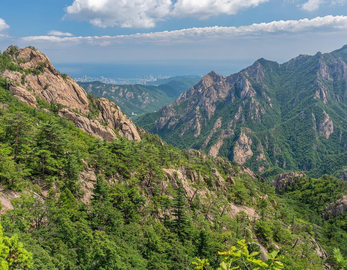 Seoraksan mountain panorama showing rugged granite peaks, forested ridges and distant coastline under blue sky