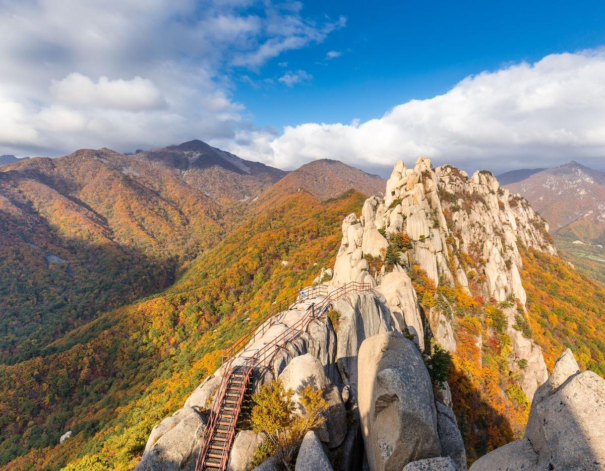 Ulsanbawi ridge with metal stairs and railings leading up jagged granite peaks, autumn foliage in Seoraksan.