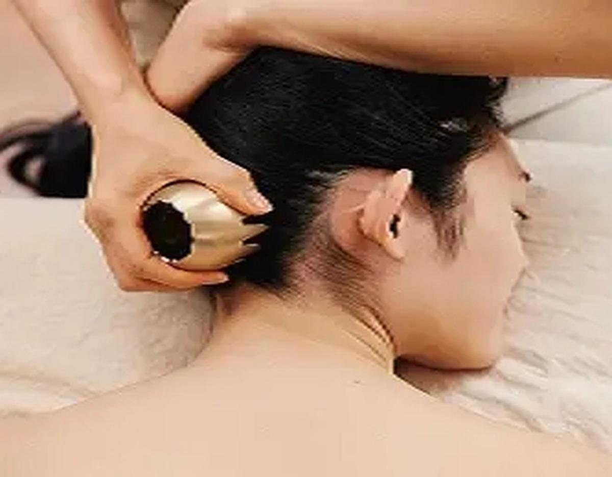 Woman lying face down receiving traditional bangjja gualsa metal tool massage on neck at 여용국 한방스파.