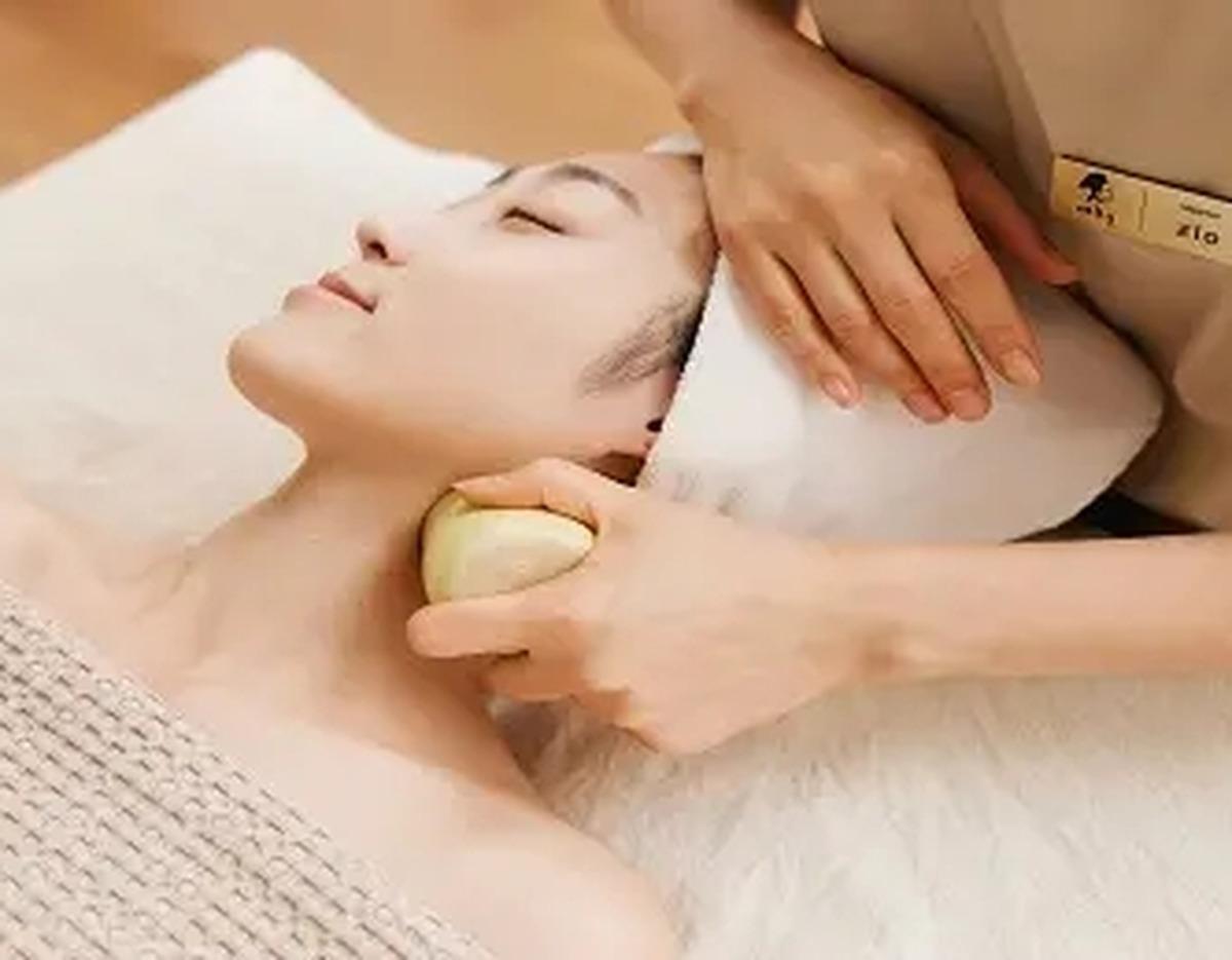 Woman receiving traditional Korean facial and neck therapy using a smooth round ceramic tool at 여용국 한방스파.