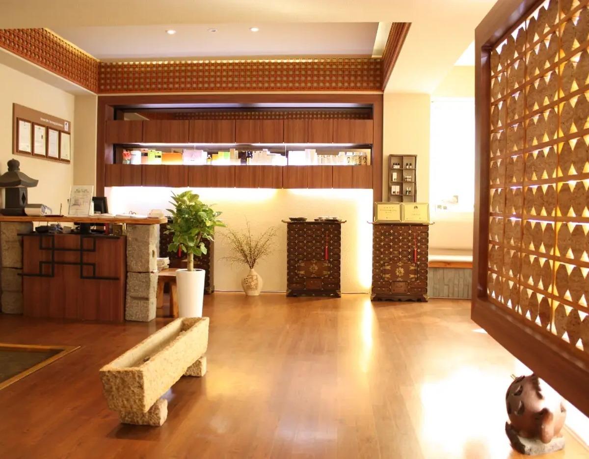 [서울] 여용국 한방스파 reception area with wooden floor, traditional Korean lattice screen, antique chests and potted plants