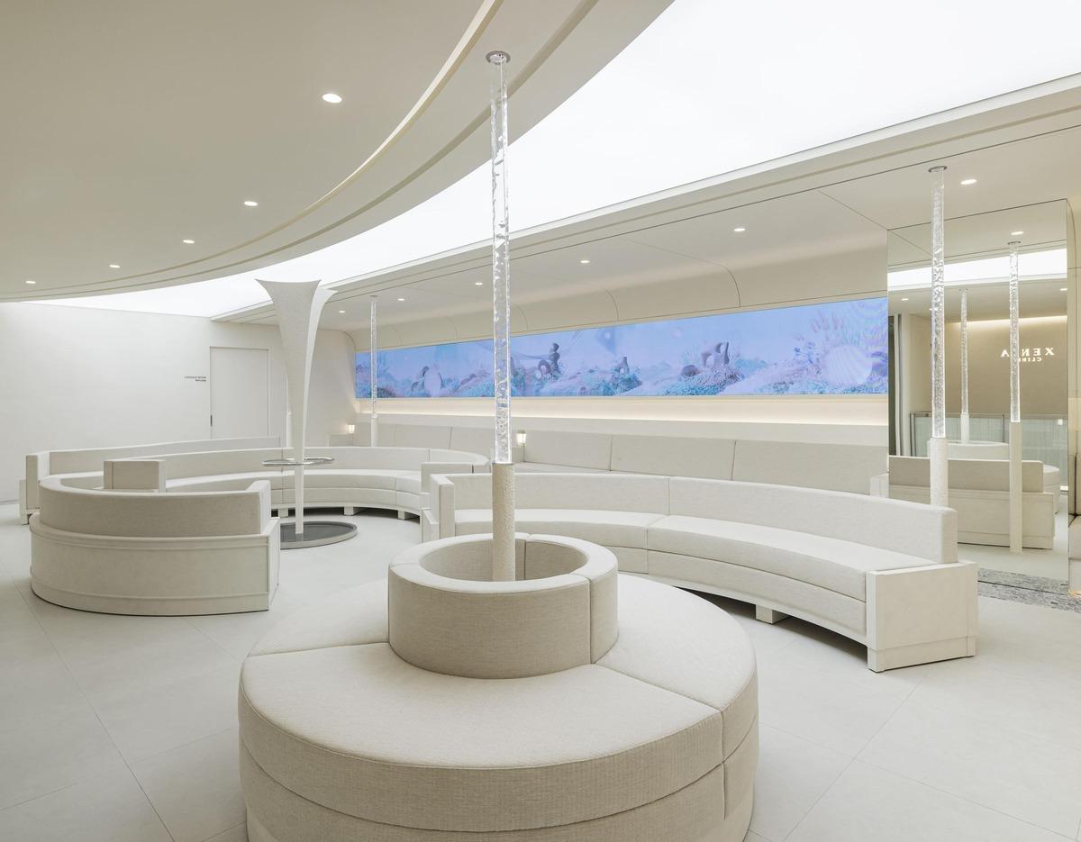 세니아의원 sleek white curved waiting area with circular beige sofas and illuminated ceiling strip