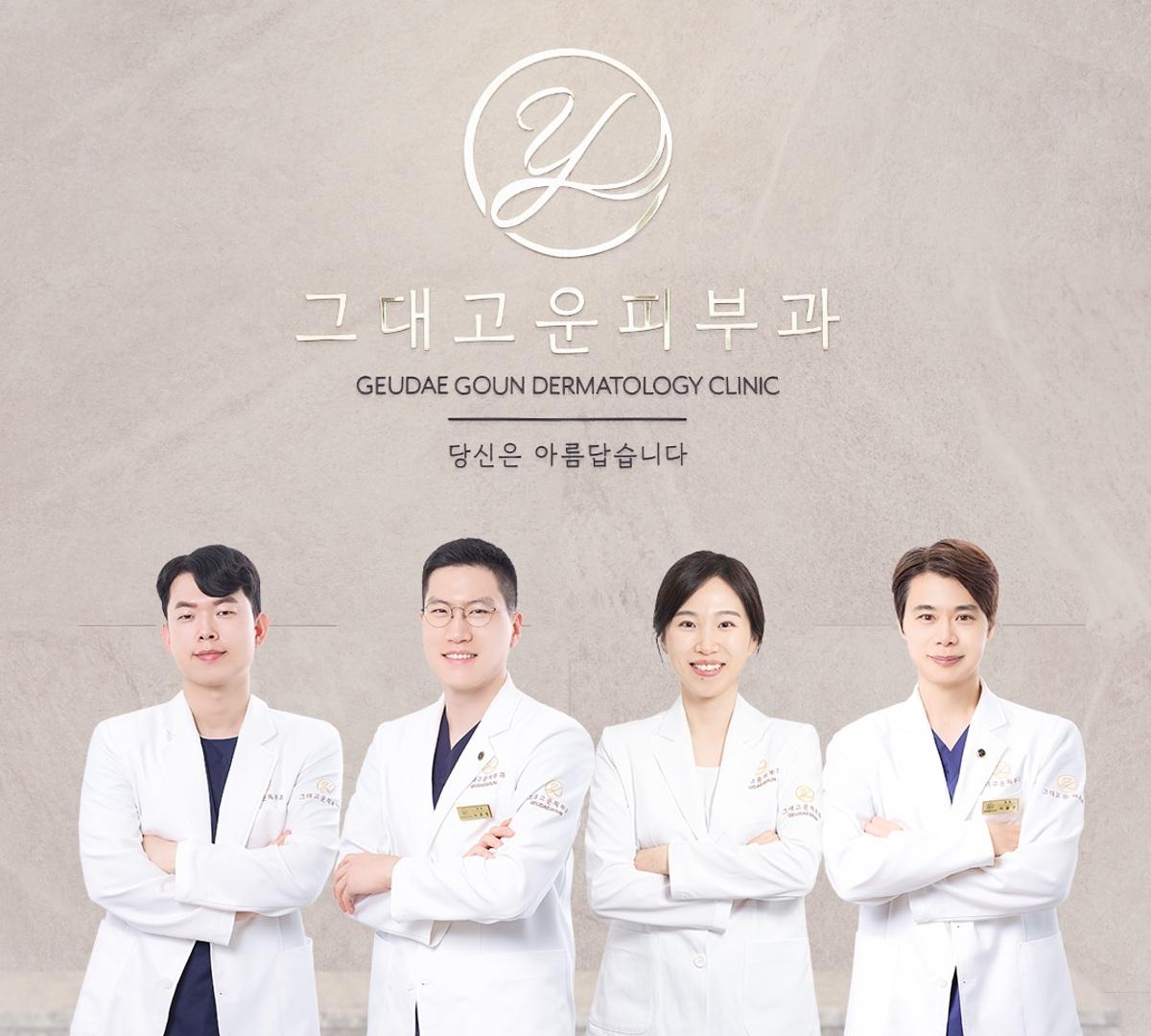 Four dermatologists in white coats standing with arms crossed under "그대고운피부과" clinic logo and English name on textured background.