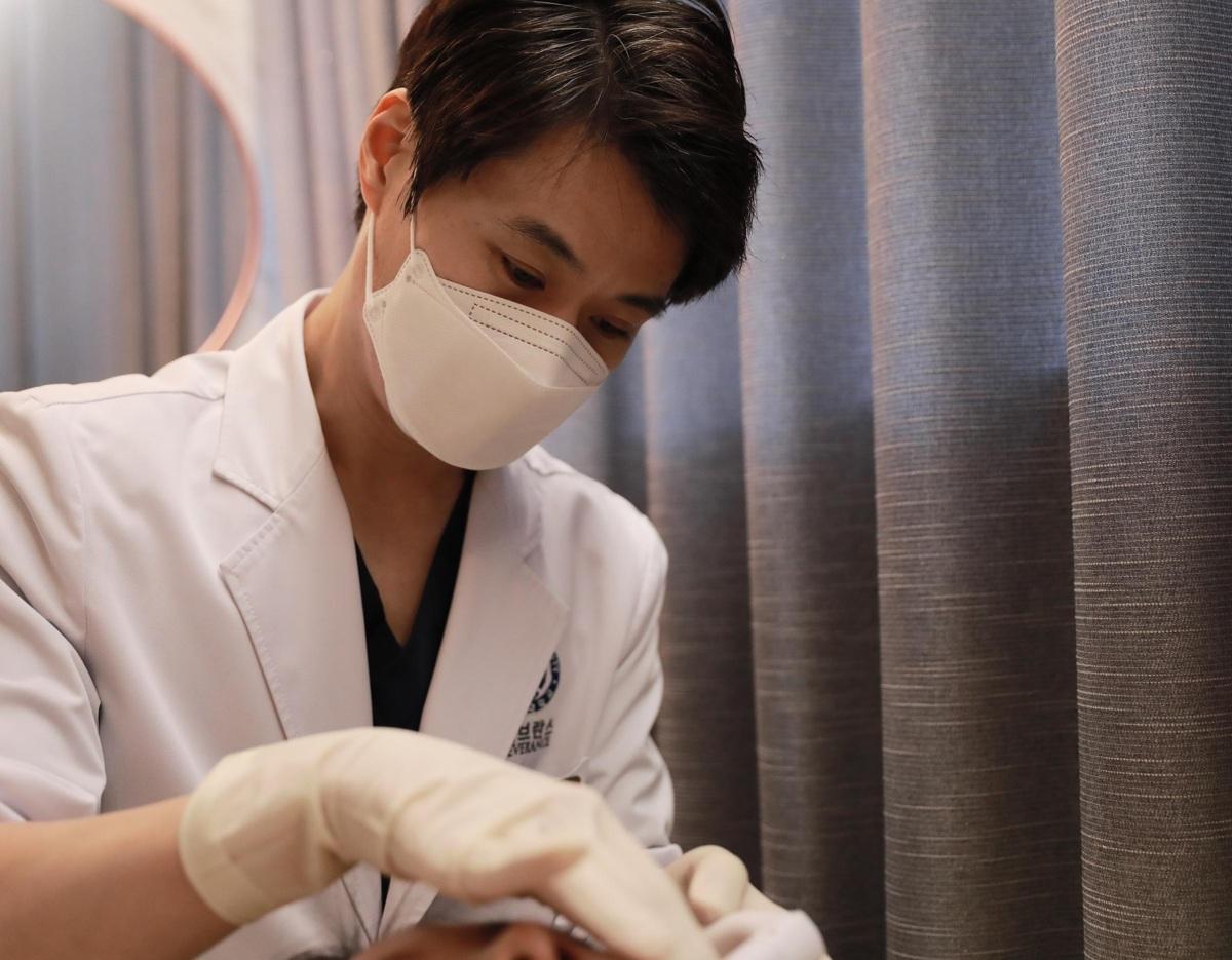 Male clinician in white coat and mask wearing gloves performing a close-up facial treatment on a patient