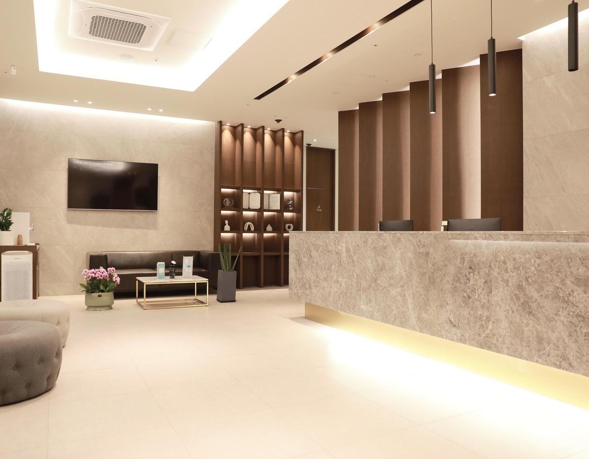 그대고운피부과의원 reception area with marble front desk, seating area, TV, decorative shelving and soft warm lighting
