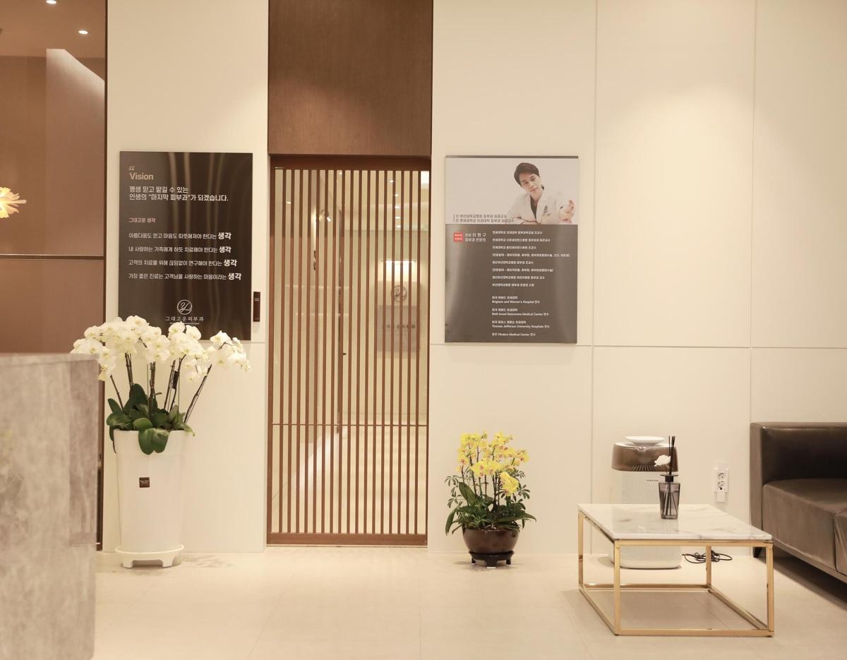그대고운피부과의원 reception area with wooden slatted door, white orchids in pot, small table and seating on beige floor