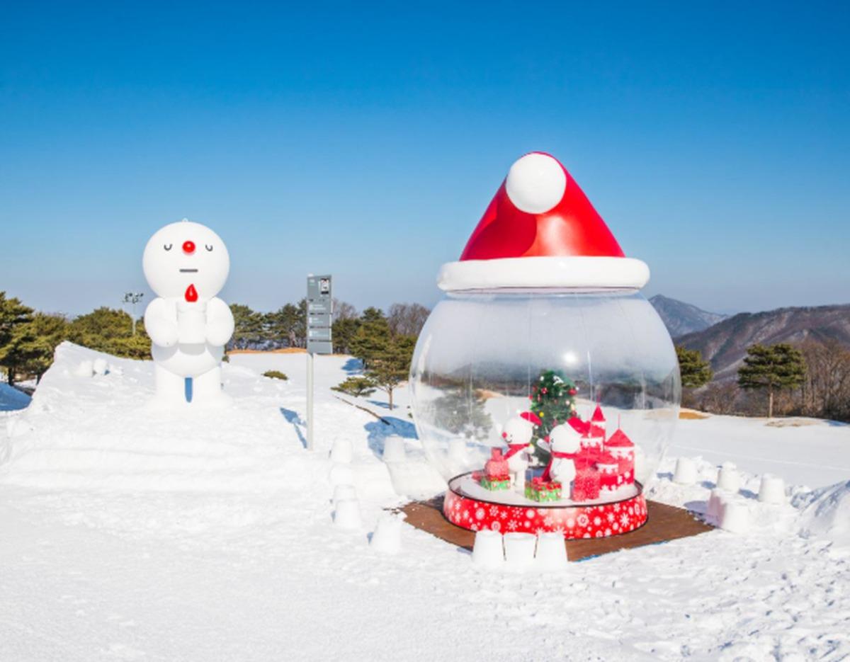Snowy resort scene at Vivaldi Park Snowyland with giant Santa hat snow globe and large cartoon snowman on slope.