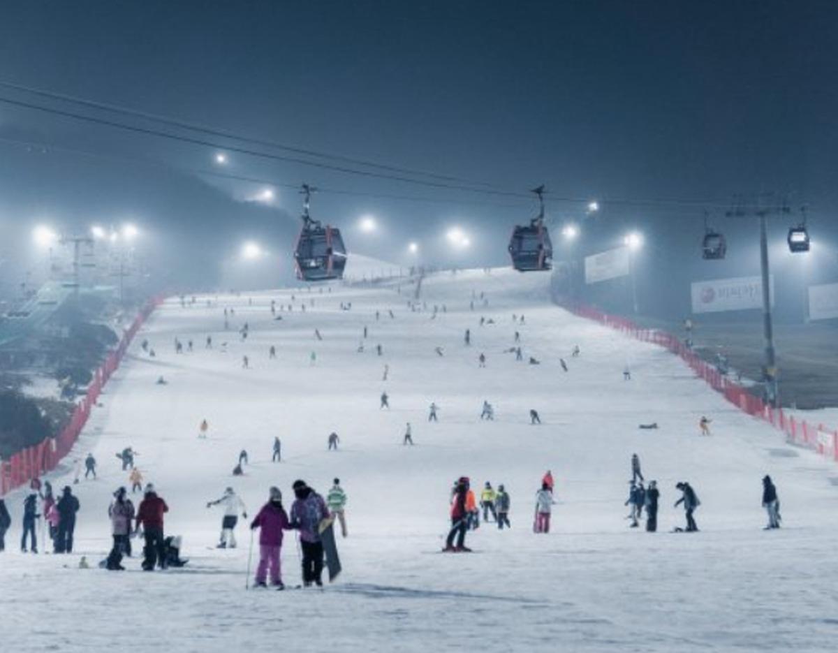 Vivaldi Park night ski slope with gondolas overhead and skiers and snowboarders scattered on lit snowy run