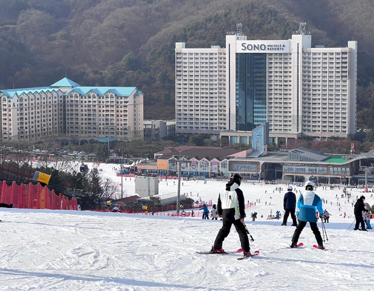 Skiers on a snowy slope with SONO Vivaldi Park resort hotel and ski village buildings in the background at Hongcheon Vivaldi Park