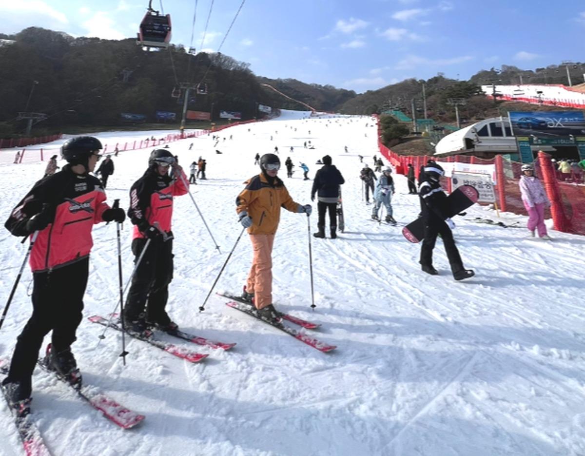 Skiers and snowboarders on a wide snowy Vivaldi Park slope with gondola lift and tree-covered hills in background