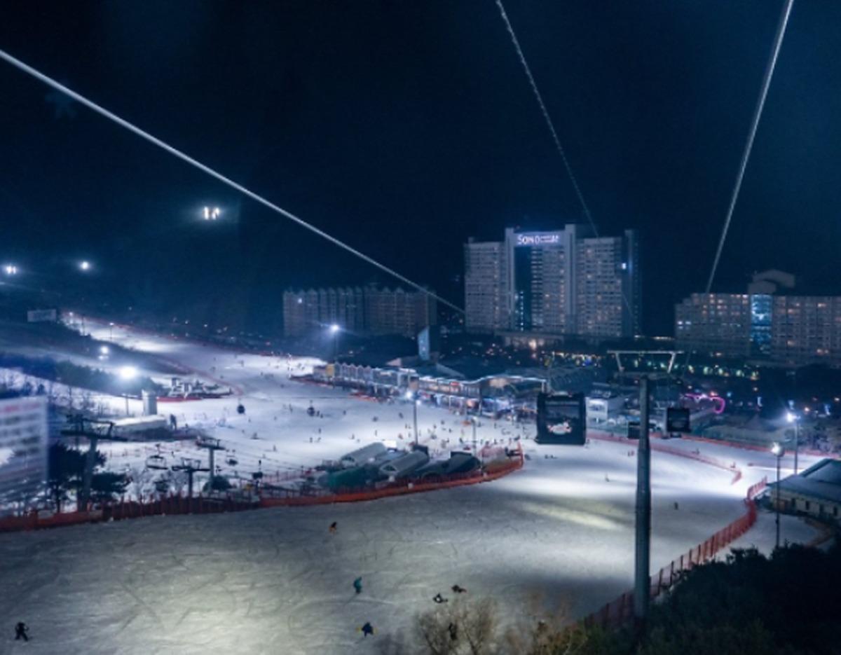 Night view of Vivaldi Park ski slopes lit up with skiers, gondola cables, and Sono Vivaldi Park hotel in background