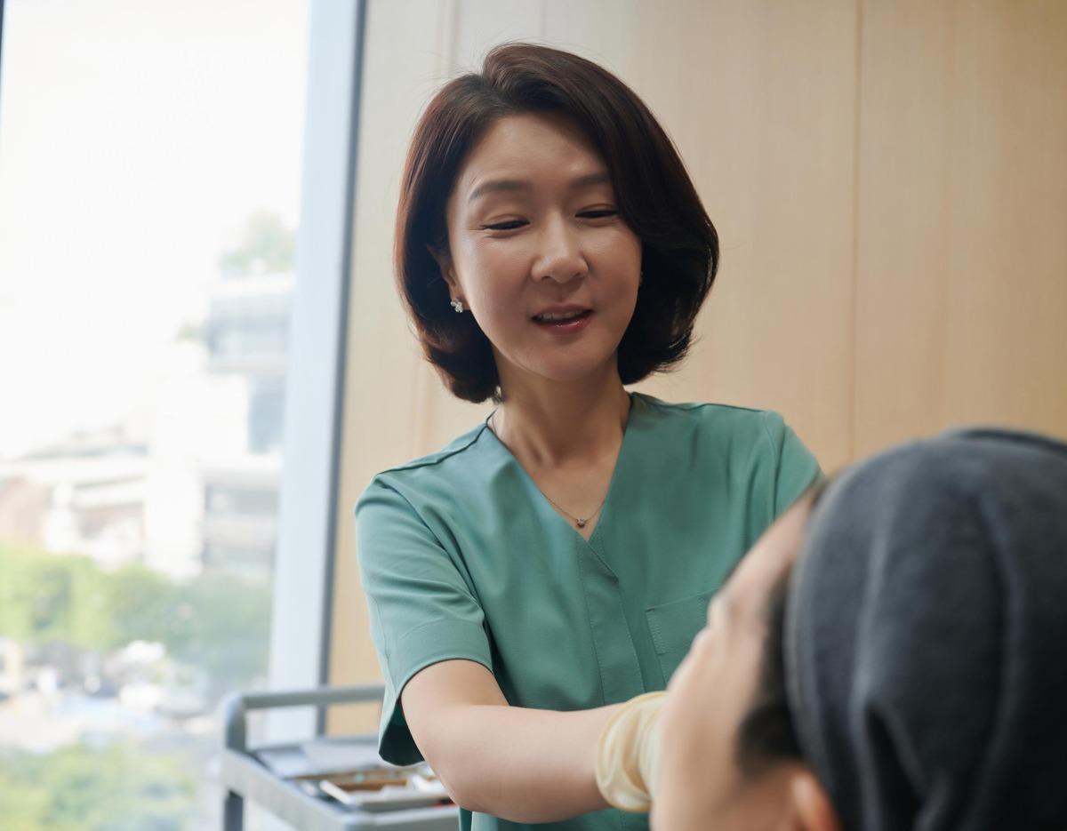 Cheongdam Na Clinic doctor in green scrubs smiling while examining a patient in a private treatment room