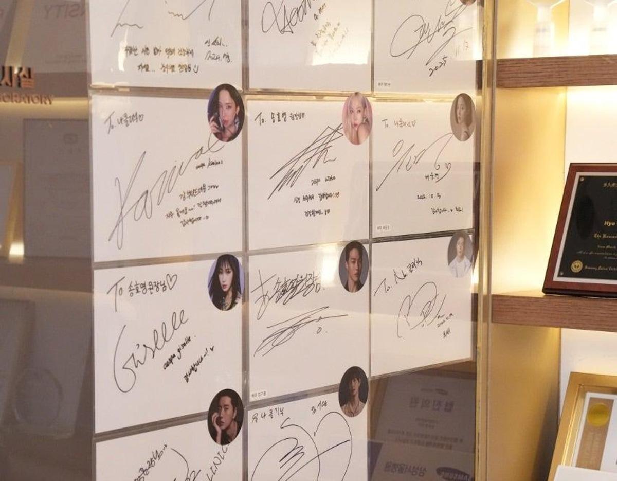 wall display of framed celebrity autograph cards with small portrait stickers arranged beside a lit wooden shelf with awards