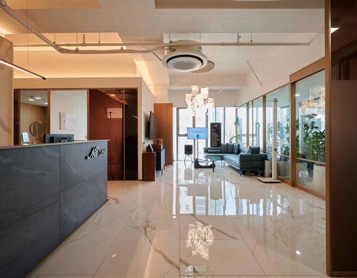 Cheongdam Na Clinic clinic reception with dark stone desk, glossy marble floor, teal sofa seating and glass-walled private rooms