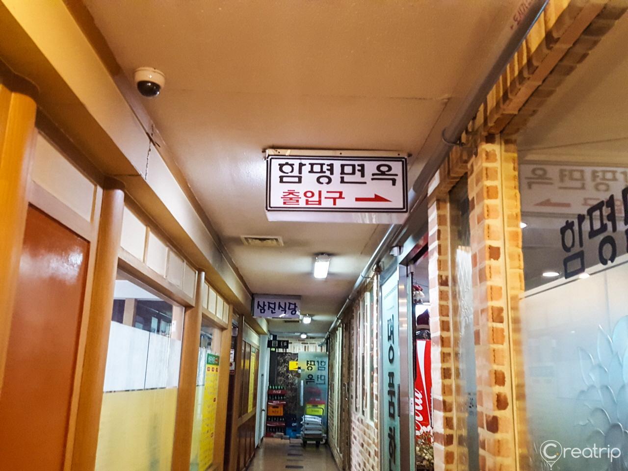 Yellow building with the name 'Hampeongmyeonok' on the sign, featuring wooden doors, gas fixtures, and a tiled ceiling, located near public transportation in a city.