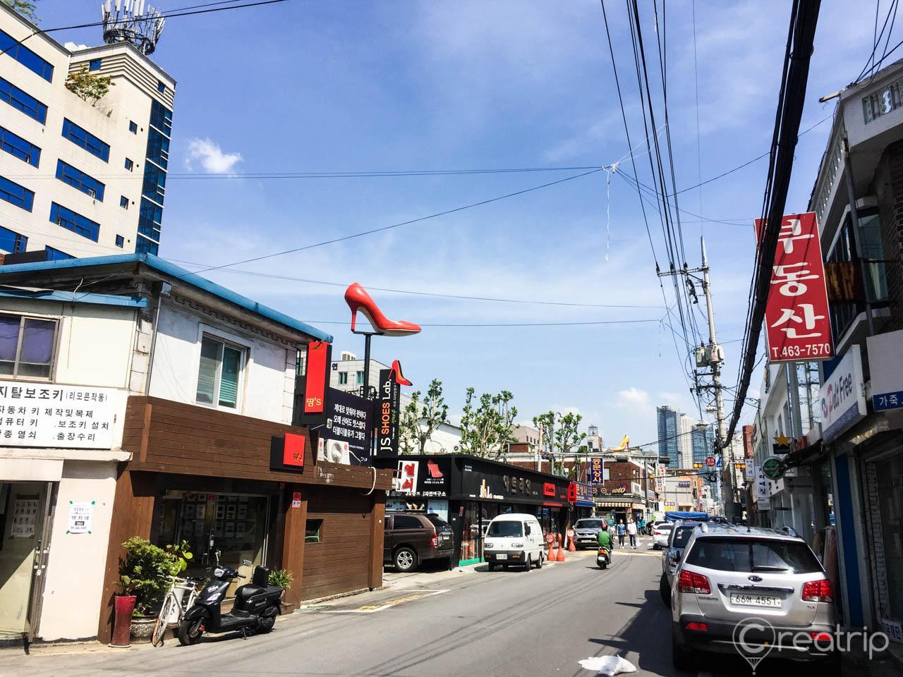 A bustling street in Seoul's trendy Seongsu-dong neighborhood featuring handcrafted shoes, cars, and buildings under a cloudy sky.