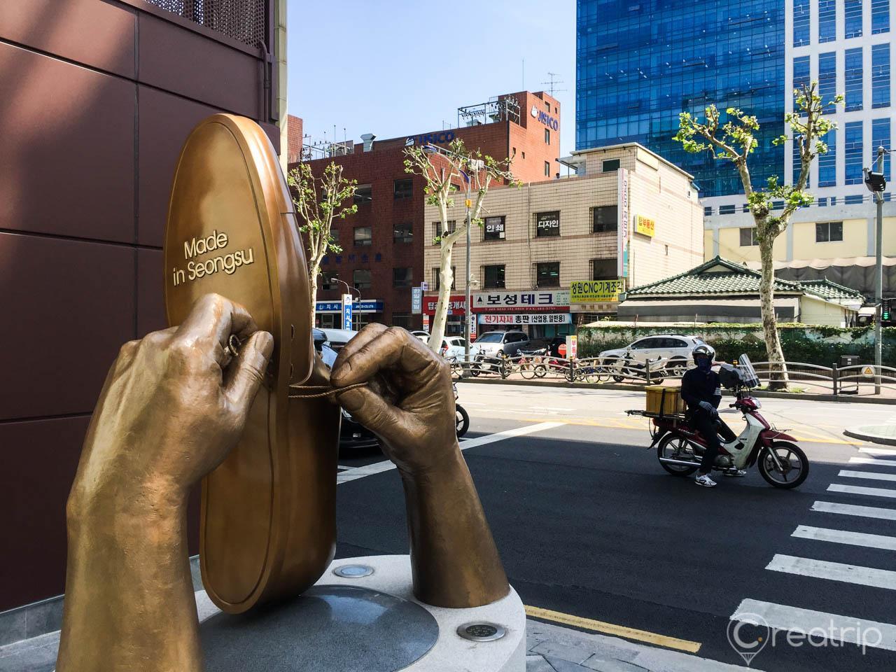 A bronze shoe sculpture stands in the handmade shoe alley of Seongsu-dong, Seoul, Korea, surrounded by buildings and vehicles.