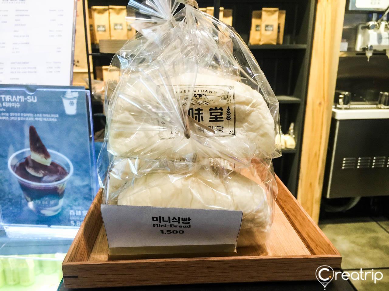 A plastic bag filled with comfort food from Baekmidang bakery in Seoul, including packed bread and wrapped cuisine.
