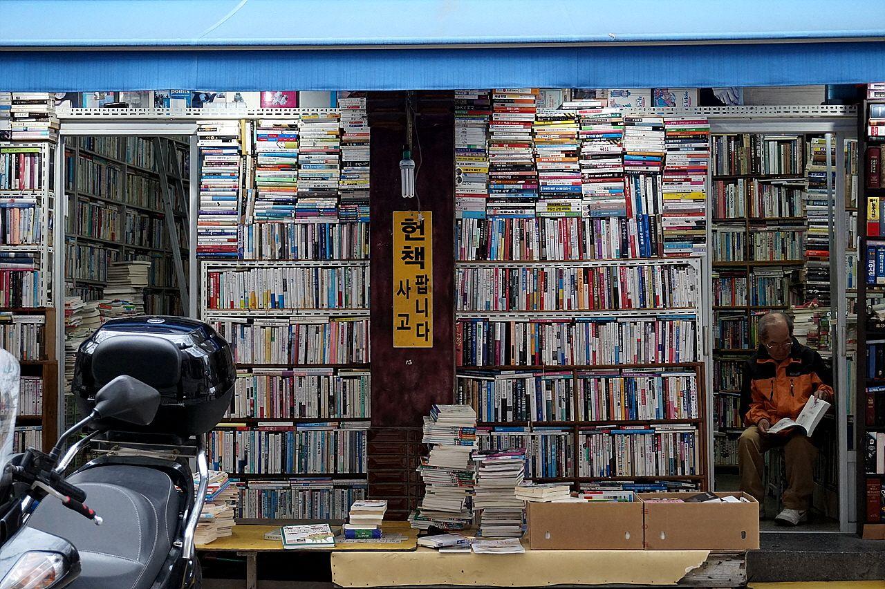 Snapshot of a book alley in Busan with shelves of publications, furniture and retail buildings in view.